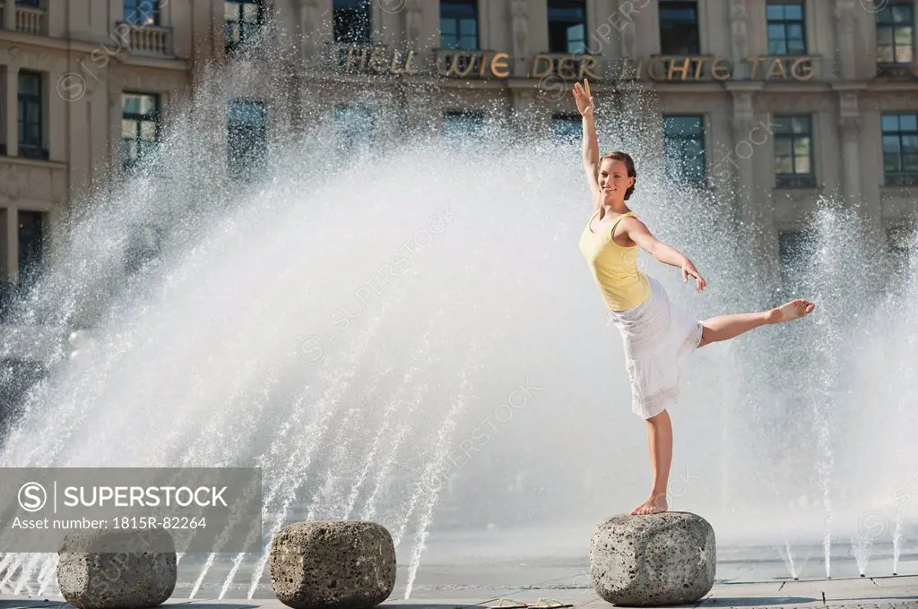Germany, Munich, Karlsplatz, Young woman standing on rock at fountain