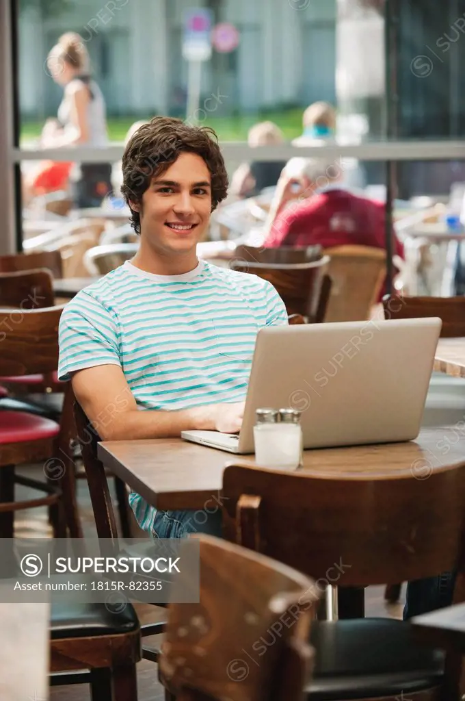 Germany, Munich, Young man with laptop in cafe, smiling, portrait