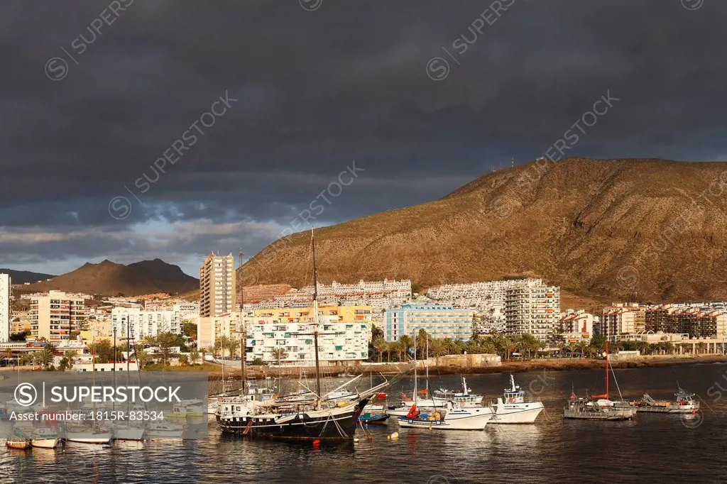 Spain, Canary Islands, Tenerife, Los Cristianos, View of boats in water with buildings and mountains in background