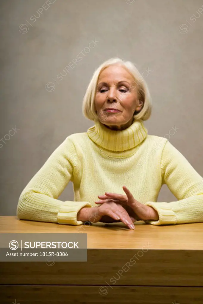 Senior woman sitting by table, looking down, close-up