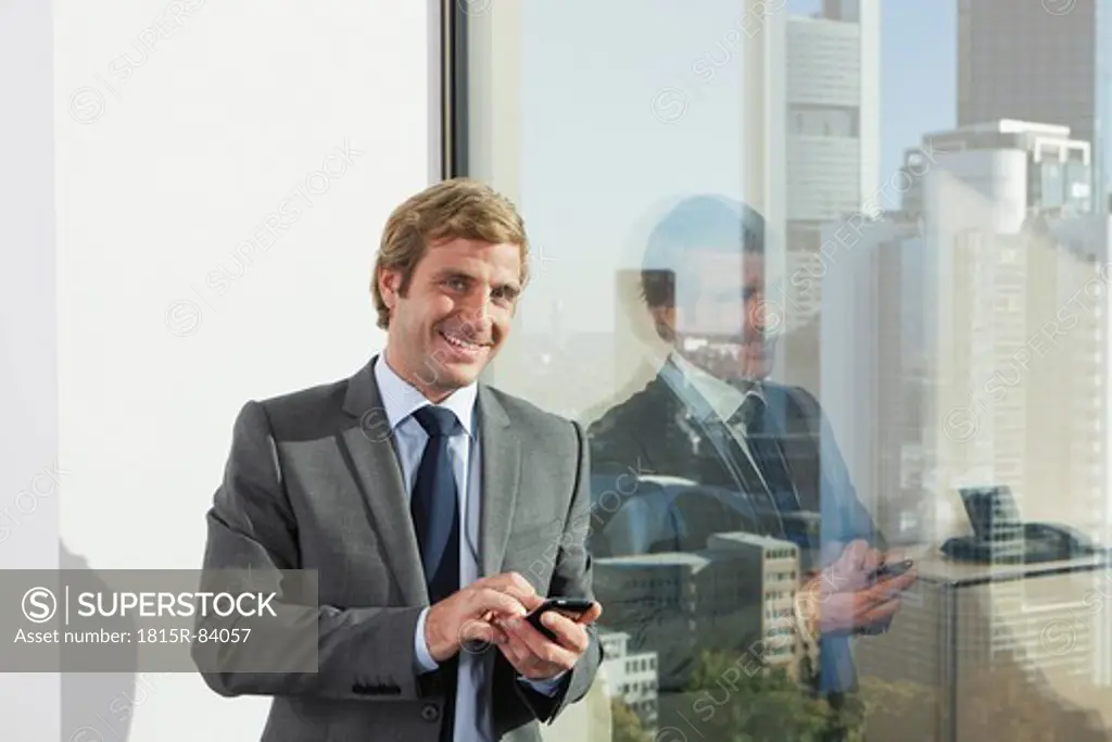 Germany, Frankfurt, Businessman using phone in office, smiling, portrait