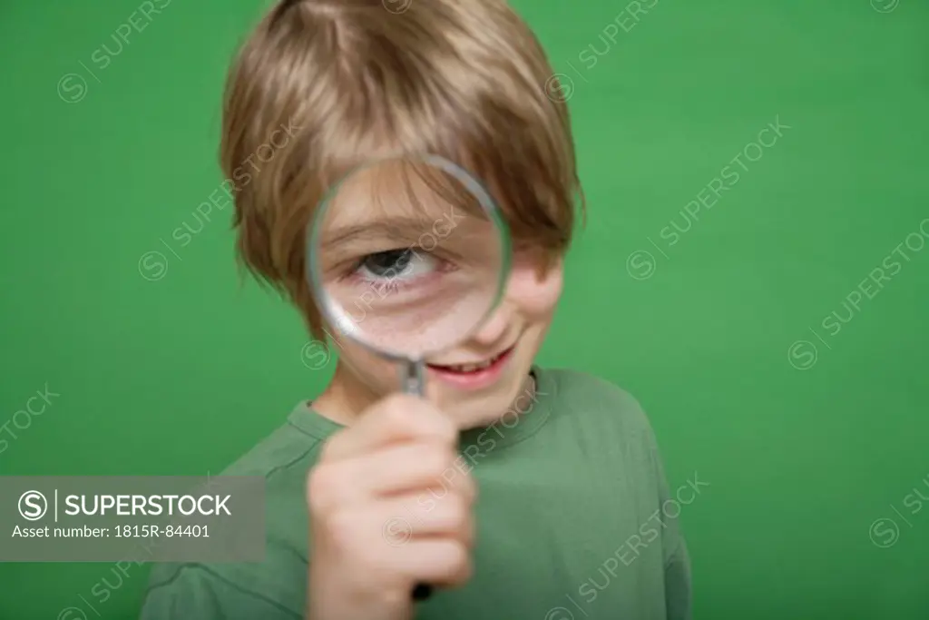 Close up of boy looking through magnifying glass against green background