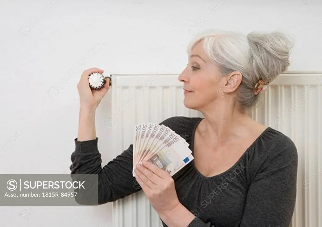 Germany, Duesseldorf, Woman holding banknotes and adjusting heater at home