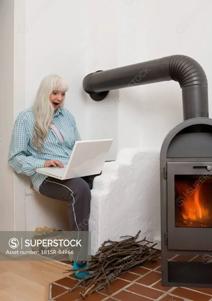 Germany, Duesseldorf, Woman using laptop near fireplace