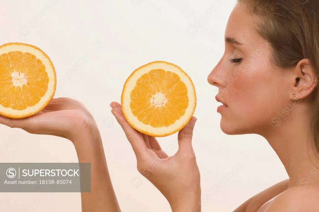 Young woman holding orange slice with eyes closed