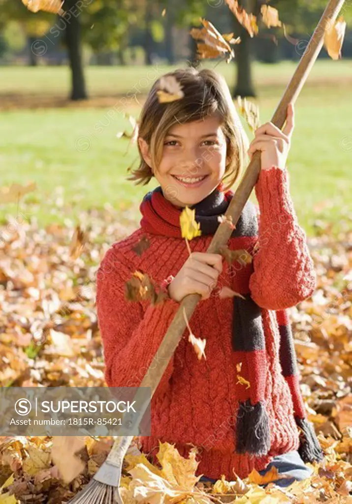 Germany, Nuremberg, Girl with rake in leaves, smiling, portrait
