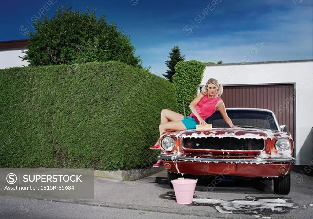Germany, Augsburg, Young woman washing her vintage car