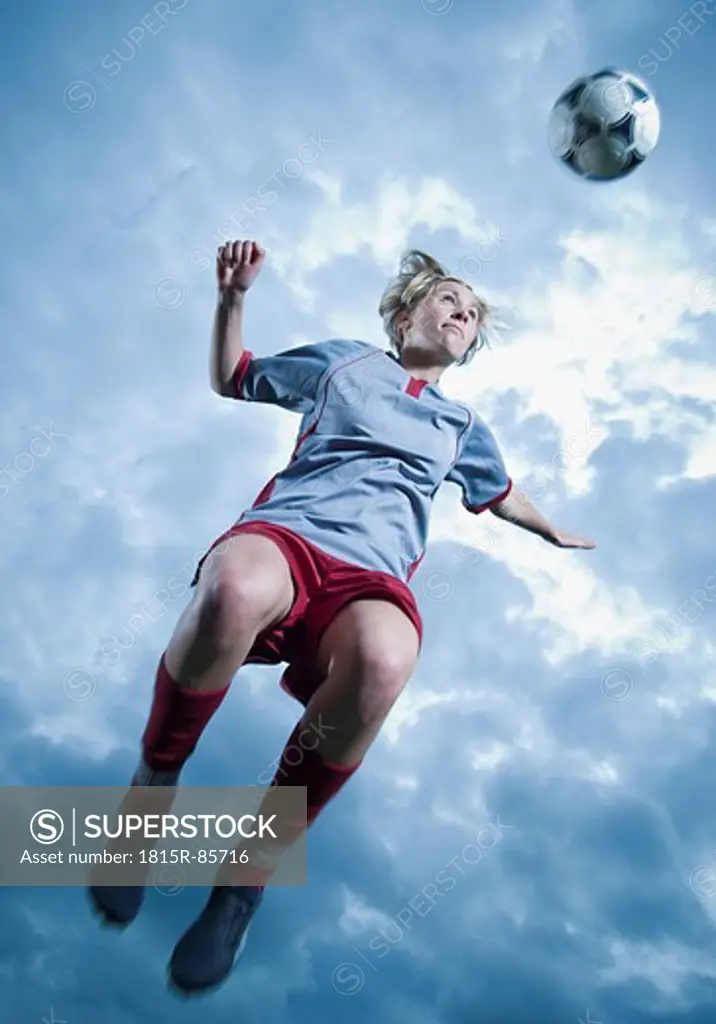 Germany, Augsburg, Soccer player jumping in the air to head a ball
