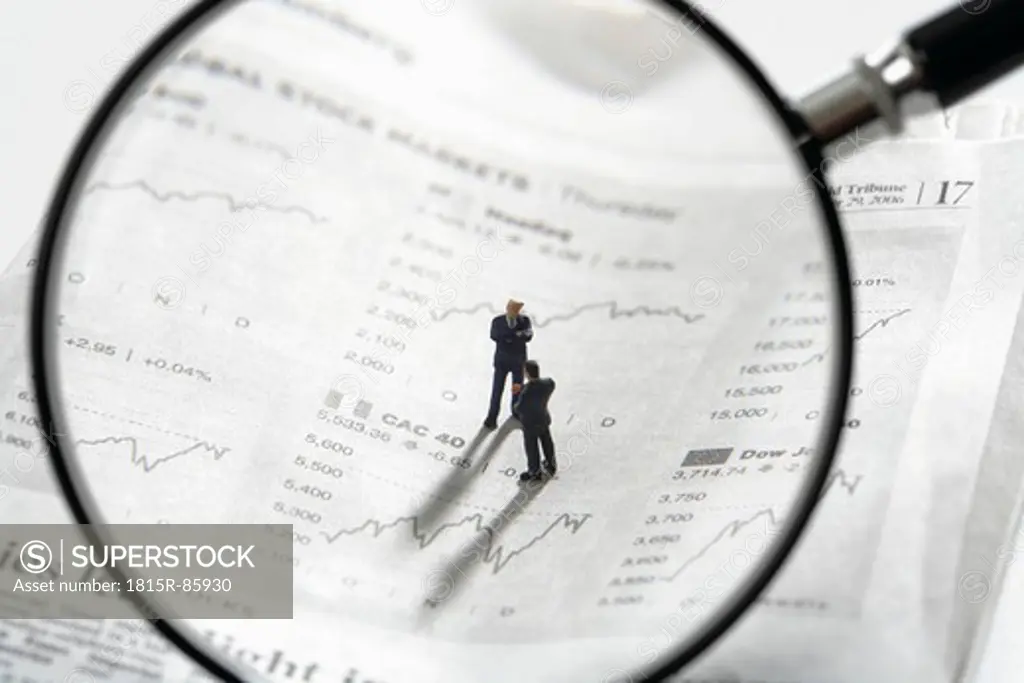 Two figurines on newspaper stock quotes with magnifying lens in foreground