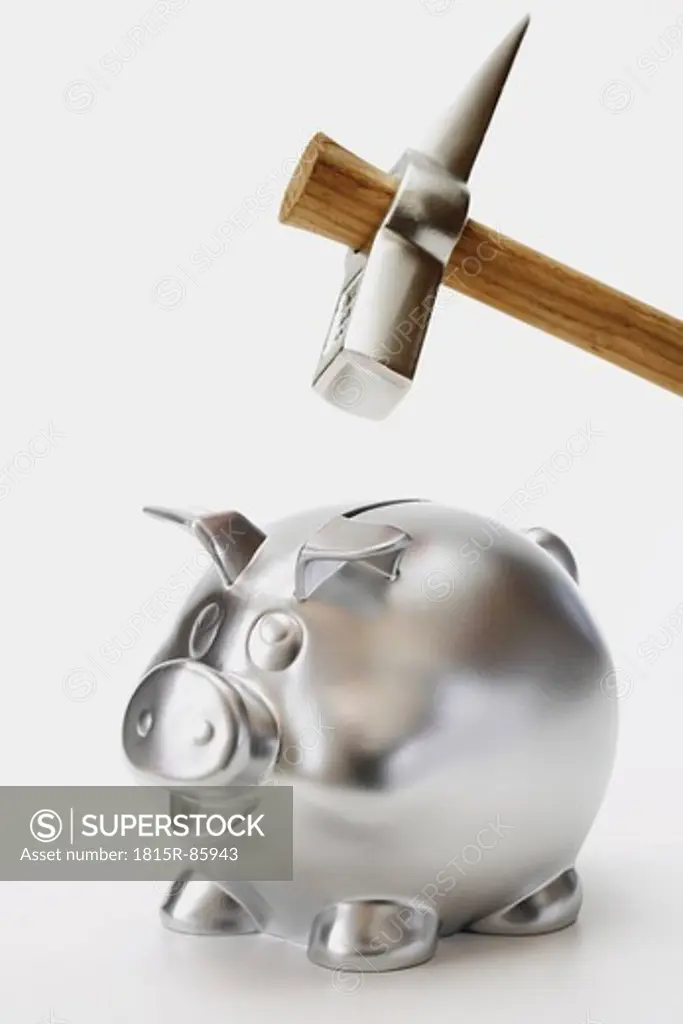 Silver piggy bank with hammer on top of it against white background, close up