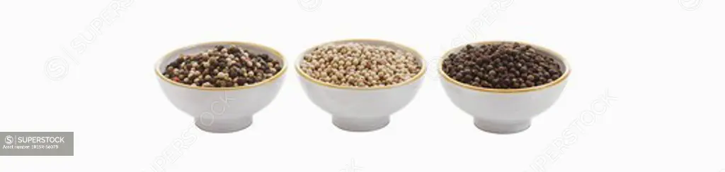 Variety of peppercorns in bowl against white background, close up