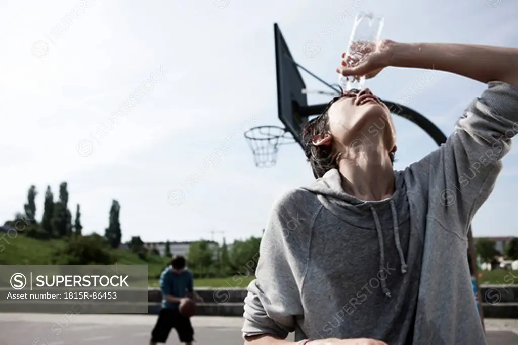 Germany, Berlin, Teenage boy pouring water on face with boy playing in background