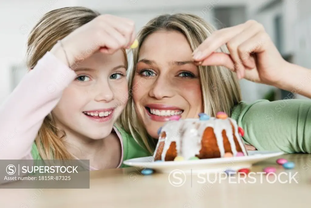 Germany, Cologne, Mother and daughter decorating cake, smiling, portrait