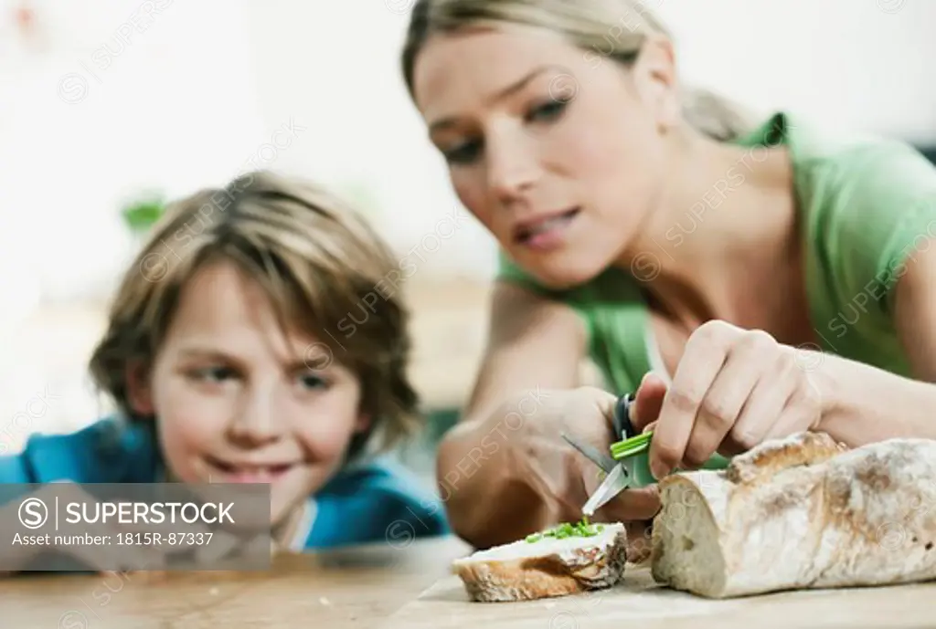 Germany, Cologne, Mother and son cutting bread in kitchen