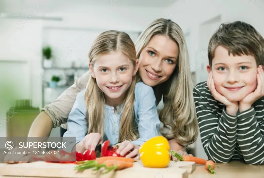 Germany, Cologne, Mother and children cutting vegetables in kitchen