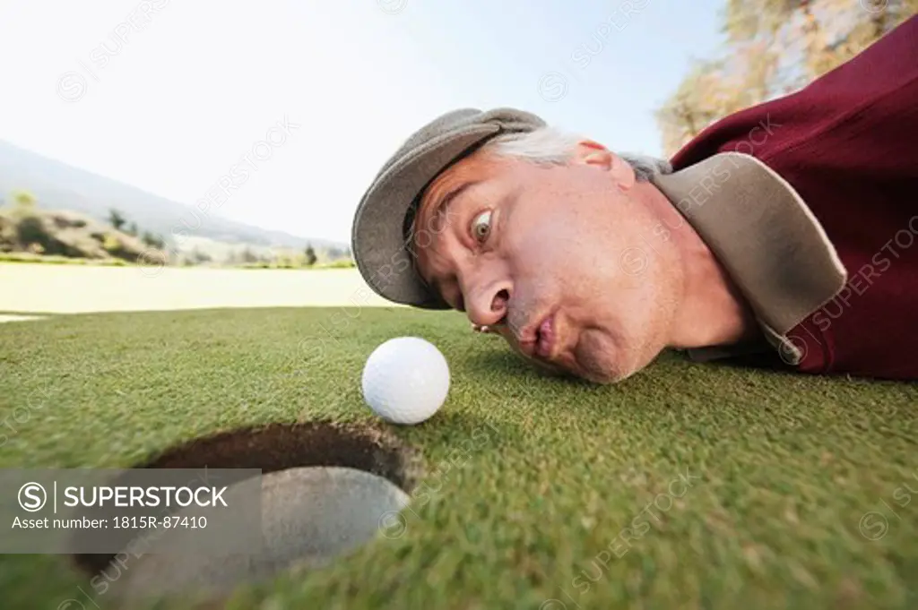 Italy, Kastelruth, Mature man blowing golf ball into hole