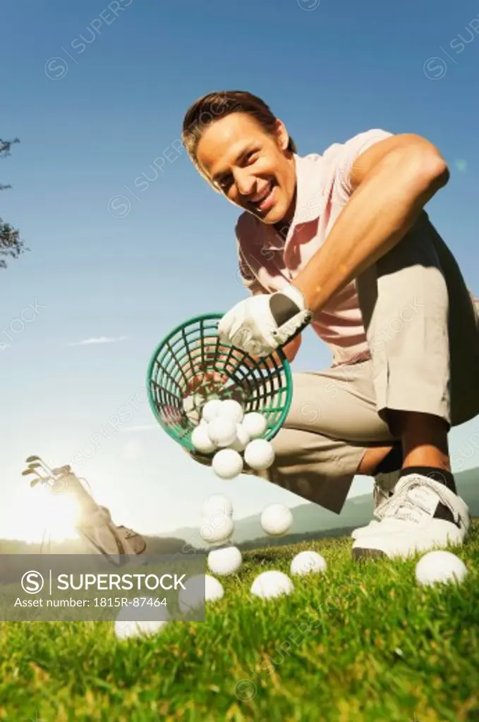 Italy, Kastelruth, Mid adult man pouring basket of golf balls on golf course