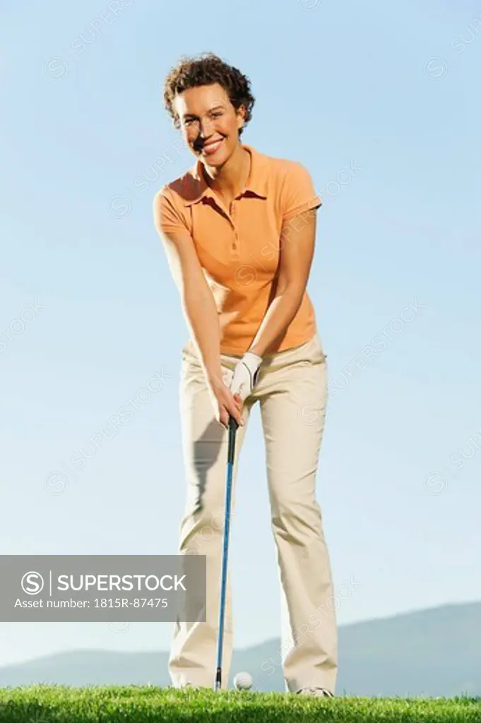 Italy, Kastelruth, Mid adult woman playing golf on golf course, smiling, portrait