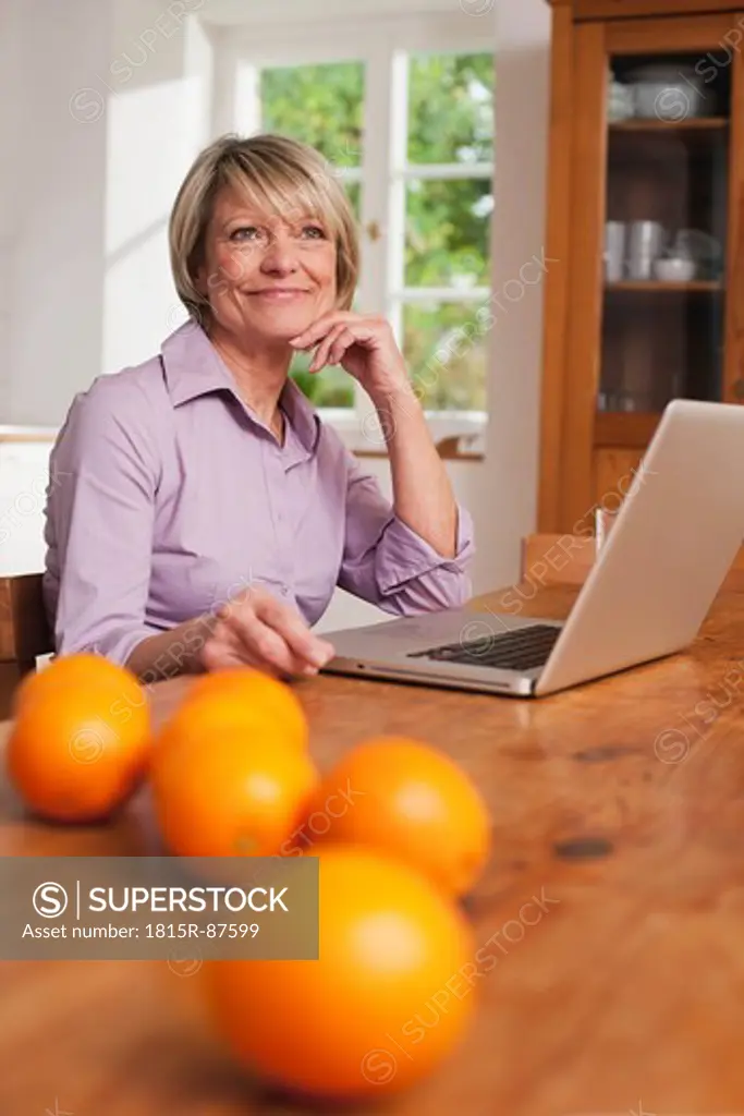 Germany, Kratzeburg, Senior woman with laptop and fruits on table in foreground