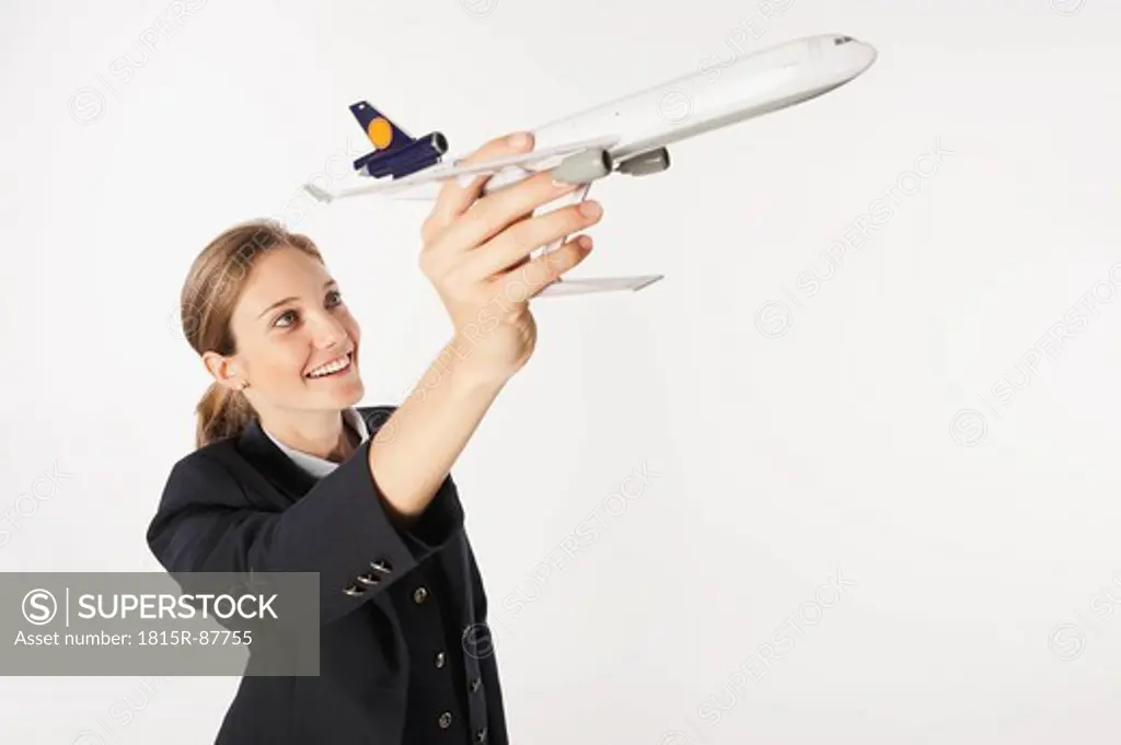 Young air stewardess with model aeroplane against white background, smiling, portrait
