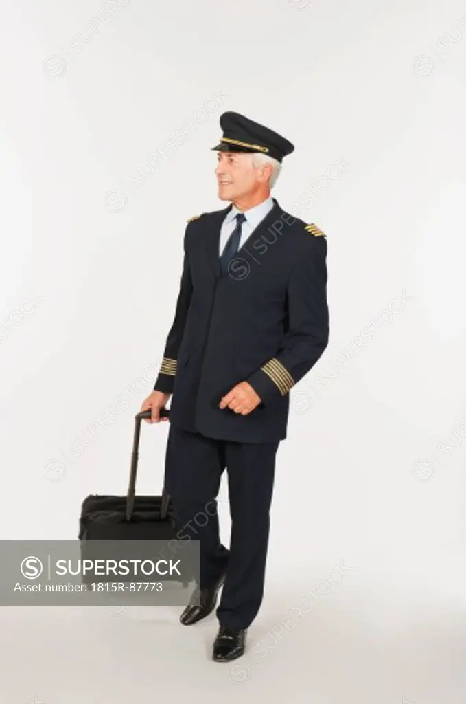 Senior flight captain carrying luggage against white background, smiling