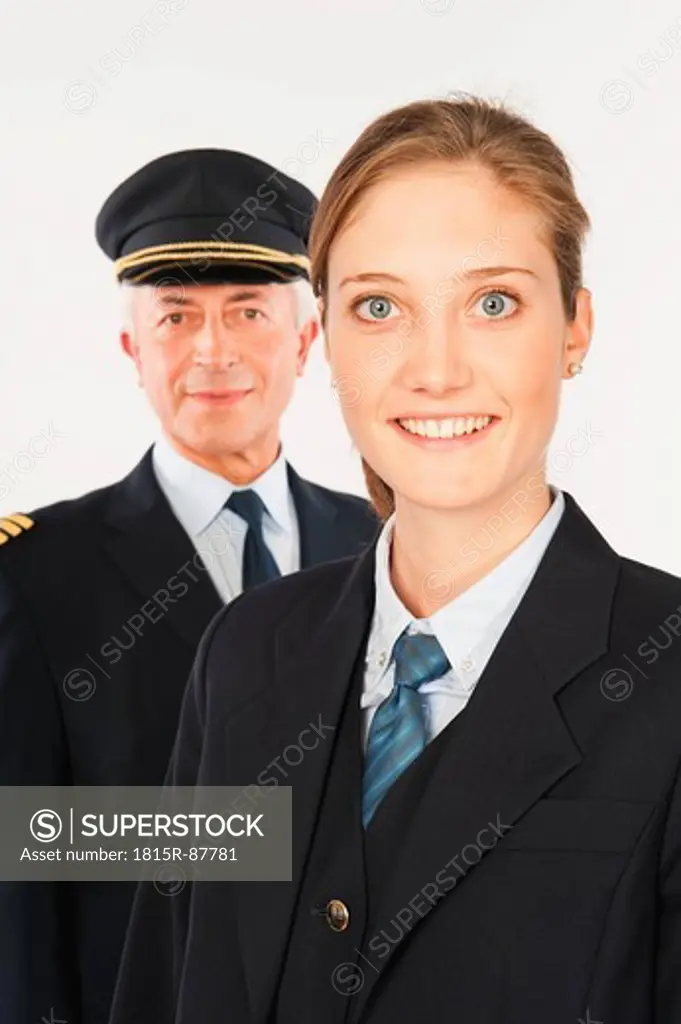 Close up of senior captain and young air stewardess against white background, smiling, portrait
