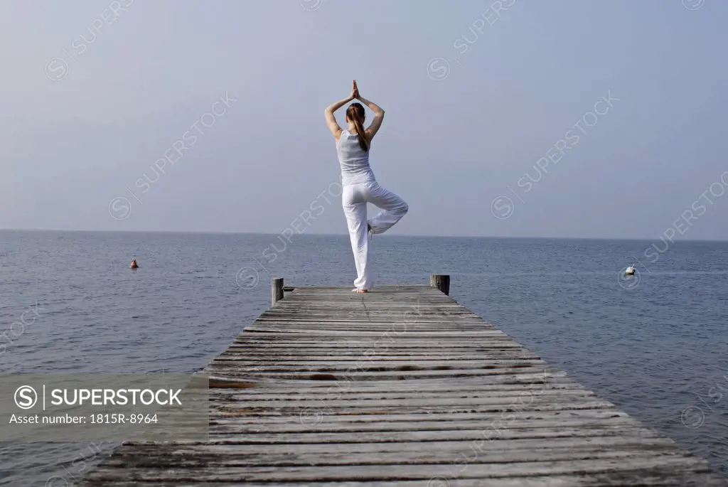 Italy, Lake Garda, Woman (20-25) exercising yoga on jetty