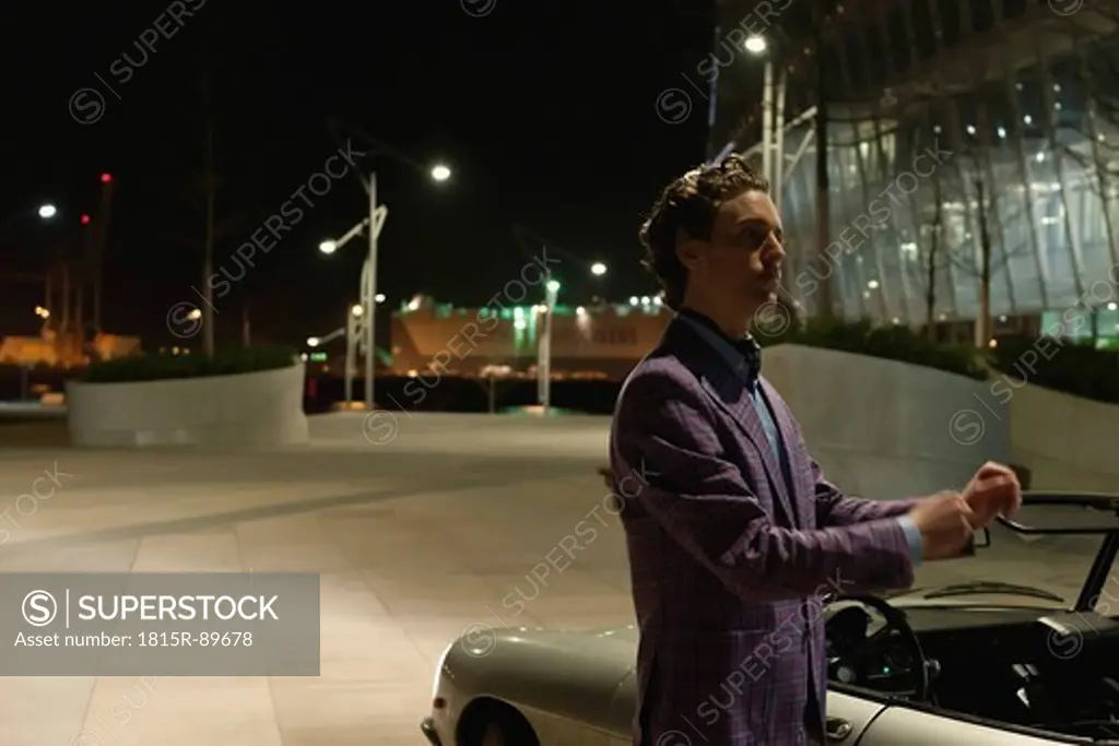 Germany, Hamburg, Man standing beside classic cabriolet car at night