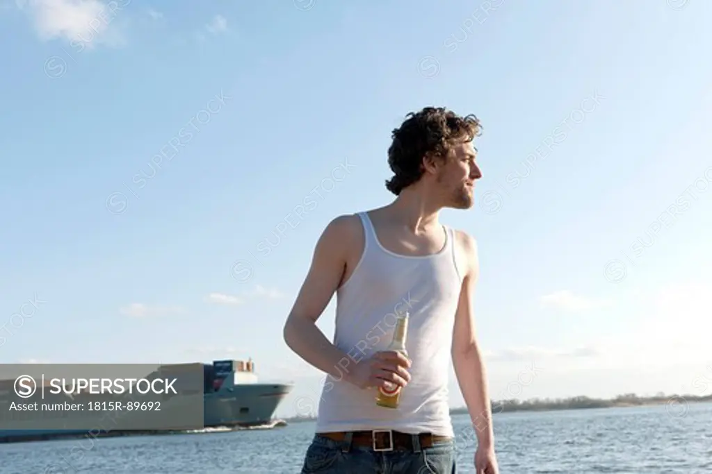 Germany, Hamburg, Man with beer bottle near Elbe riverside and container ship in background