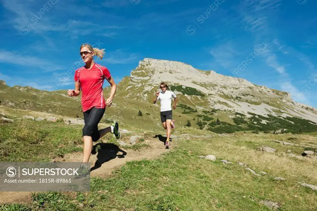 Austria, Kleinwalsertal, Man and woman running on mountain trail