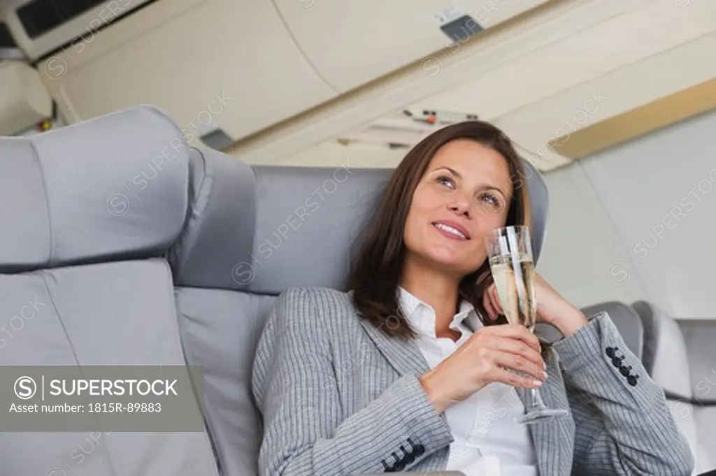 Germany, Bavaria, Munich, Mid adult businesswoman drinking champagne in business class airplane cabin