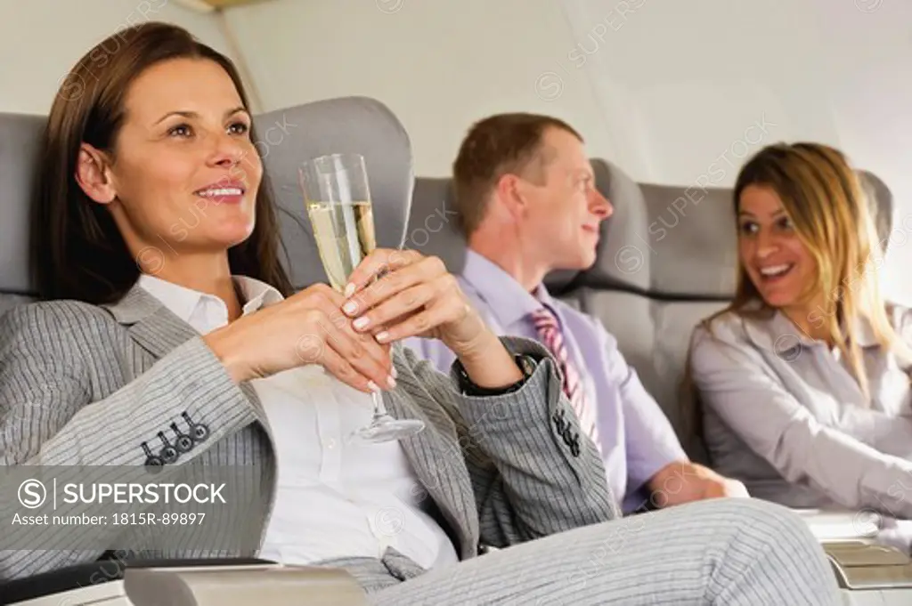 Germany, Bavaria, Munich, Business people talking and holding champagne in business class airplane cabin, smiling
