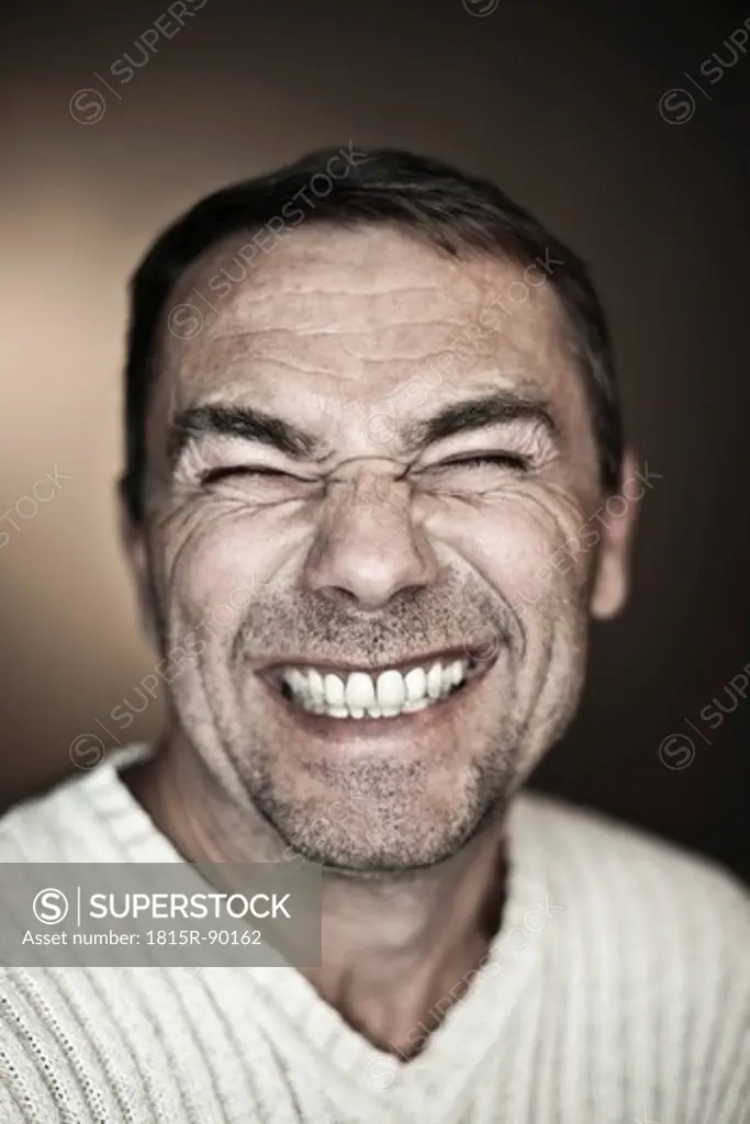Close up of mature man making funny faces against black background, smiling
