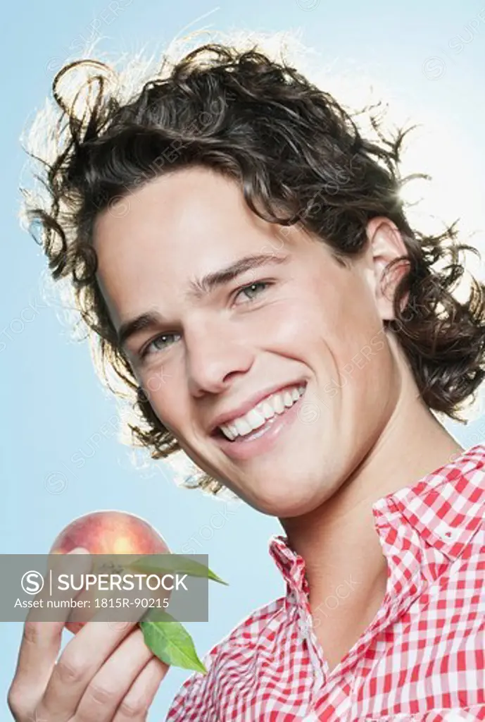 Italy, Tuscany, Close up of young man holding peach, smiling, portrait
