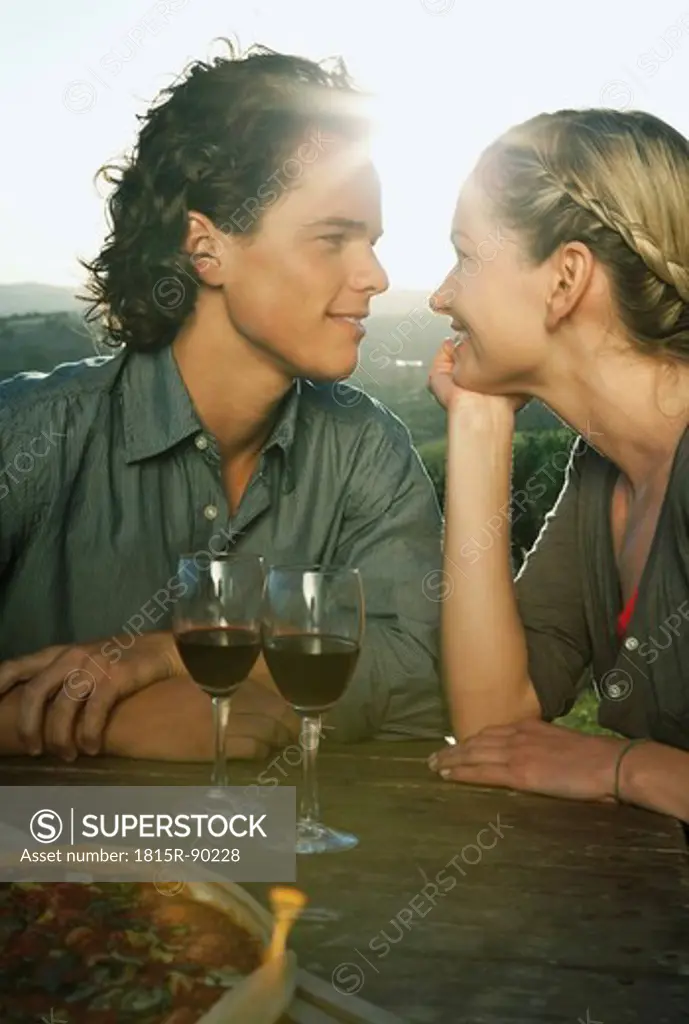 Italy, Tuscany, Young couple looking at each other with wine glasses on table at dusk