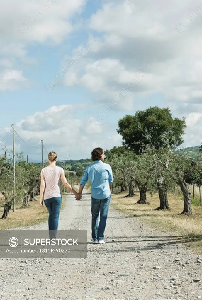 Italy, Tuscany, Young couple holding hands and walking on country road