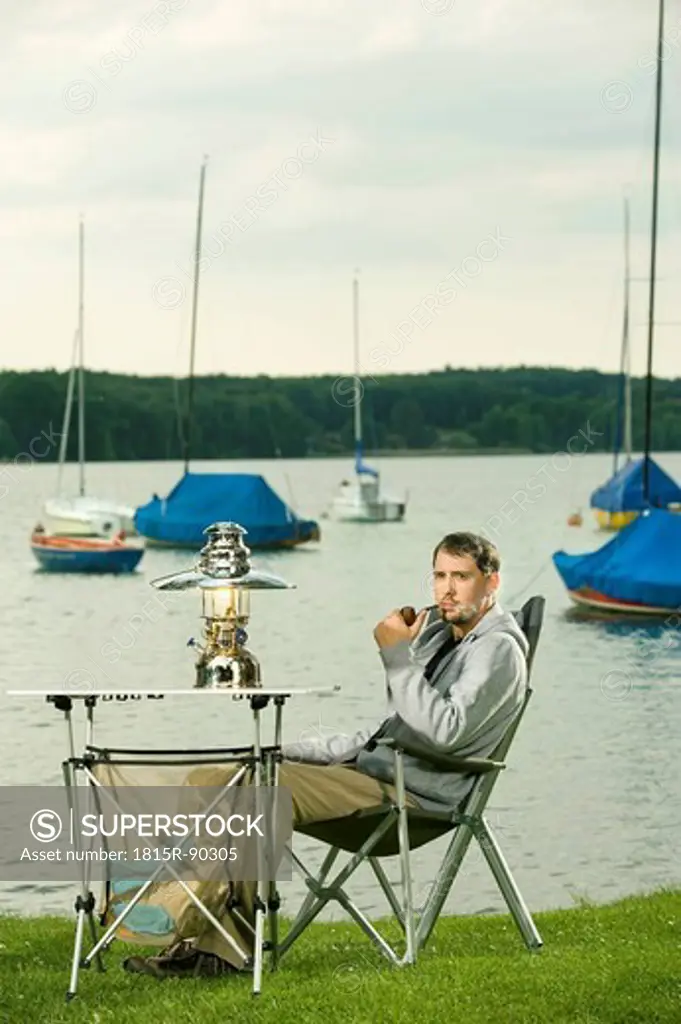 Germany, Bavaria, Woerthsee, Man smoking pipe near lakeshore while camping