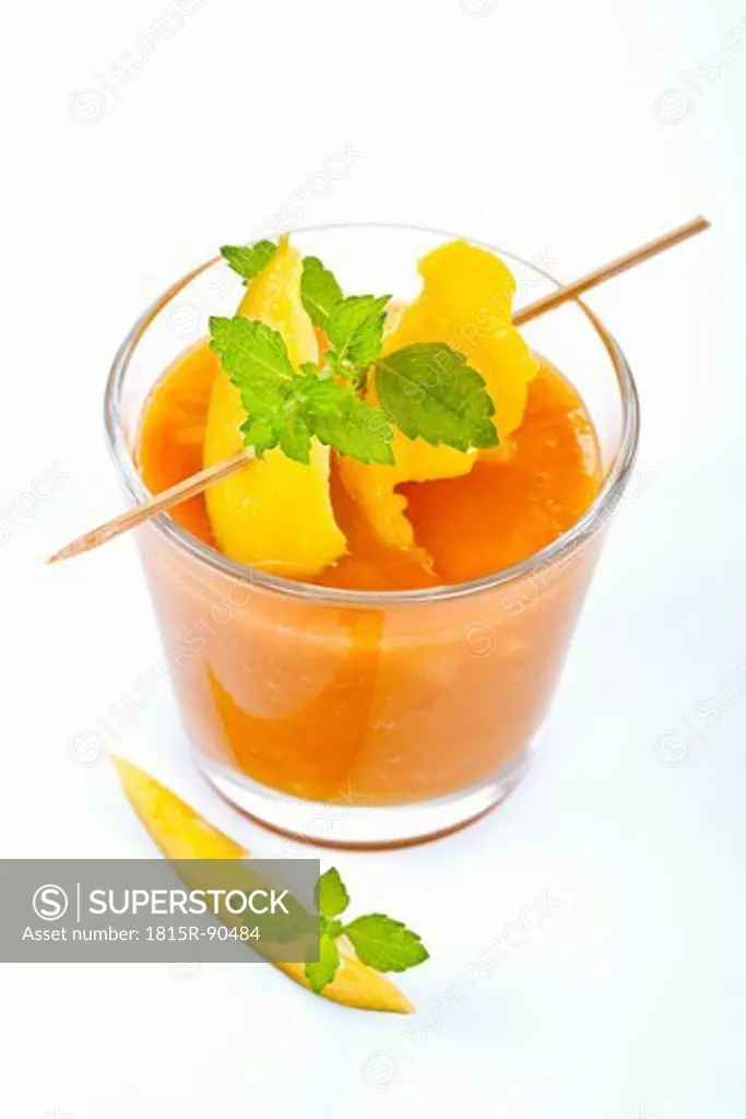 Close up of mango smoothie with mint and mango slice on white background