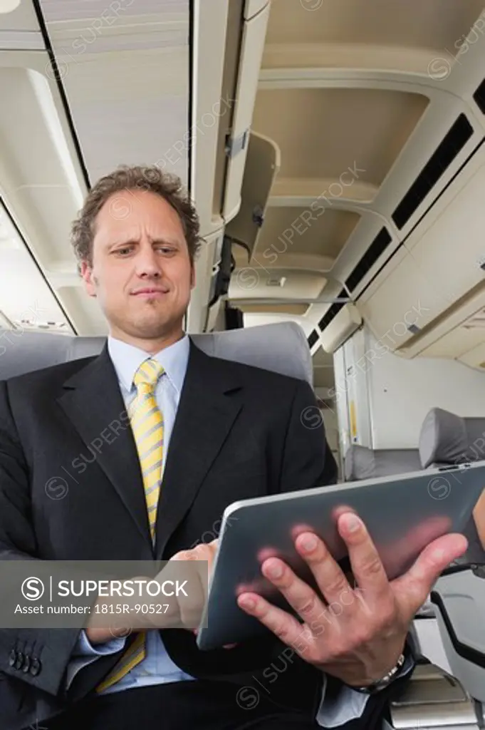 Germany, Bavaria, Munich, Businessman using ipad in business class airplane cabin