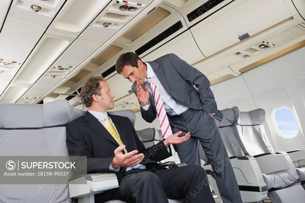 Germany, Bavaria, Munich, Businessmen whispering in business class airplane cabin