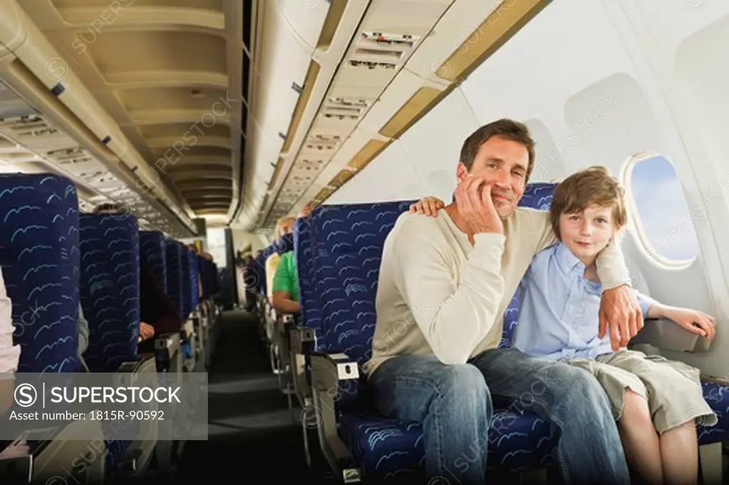 Germany, Munich, Bavaria, Man and boy sitting together in economy class airliner