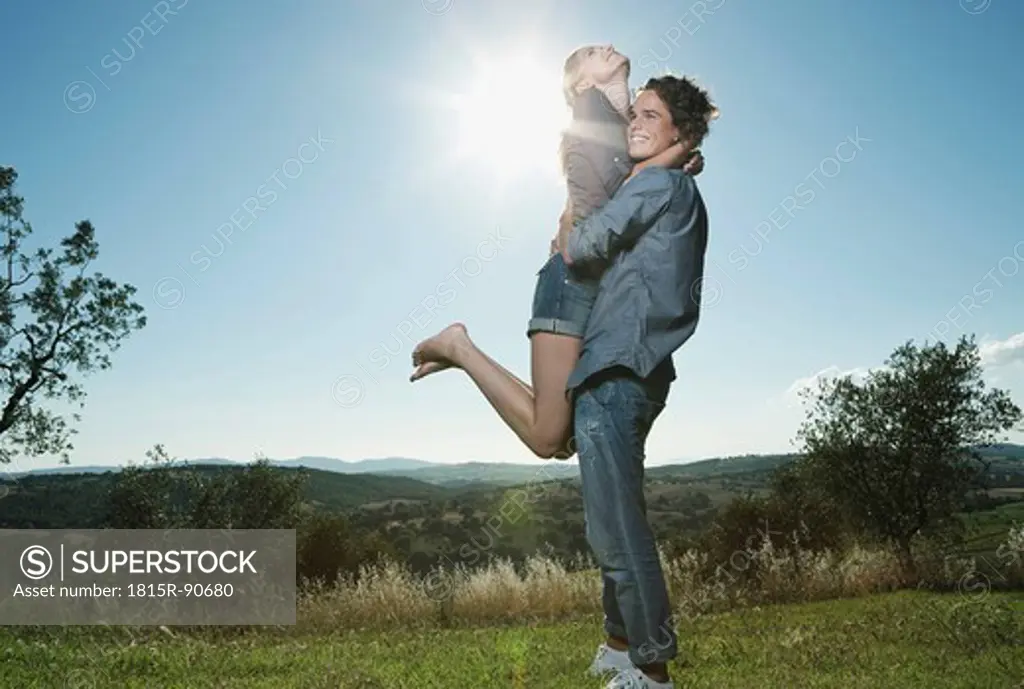 Italy, Tuscany, Young man carrying woman on his back against sun