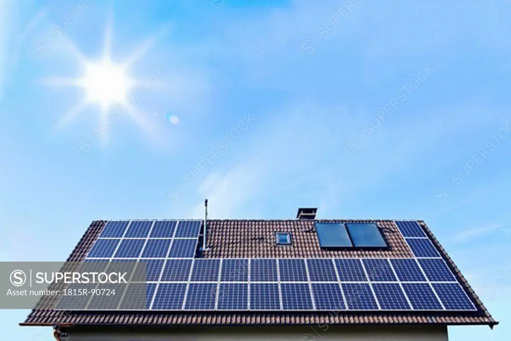 Germany, Solar panels on houseroof in front of blue sky with sun