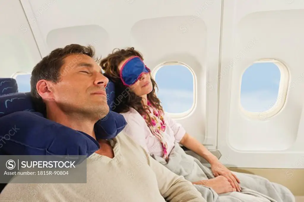 Germany, Munich, Bavaria, Mid adult couple wearing sleep mask and sleeping in economy class airliner