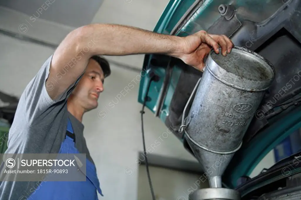 Germany, Ebenhausen, Mechatronic technician pouring oil in car at car garage