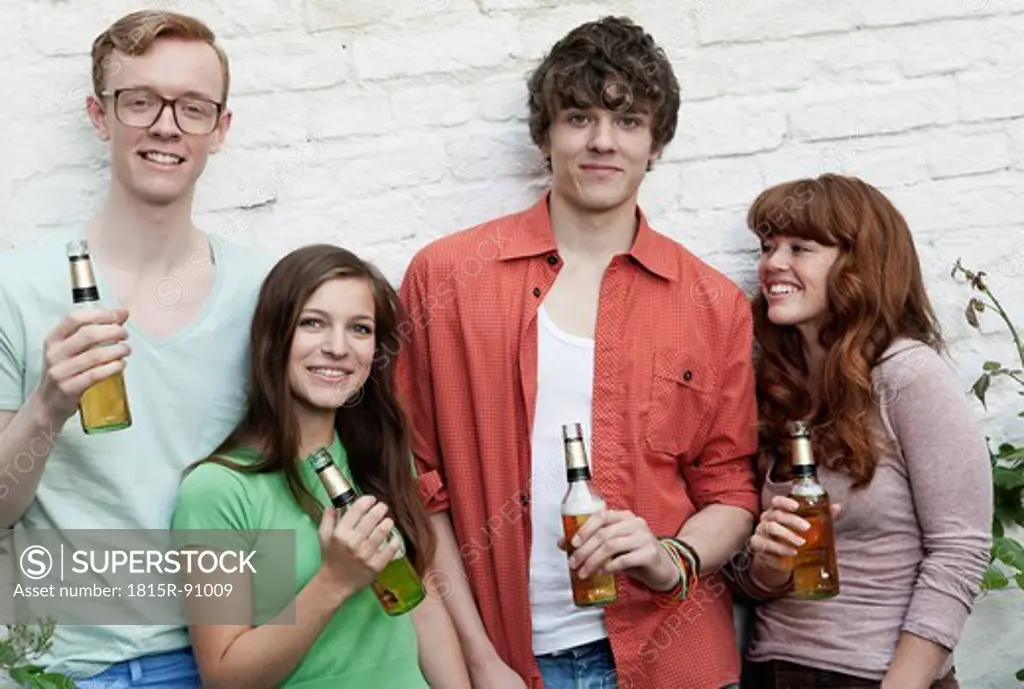 Germany, Berlin, Young men and women holding beer bottles, smiling