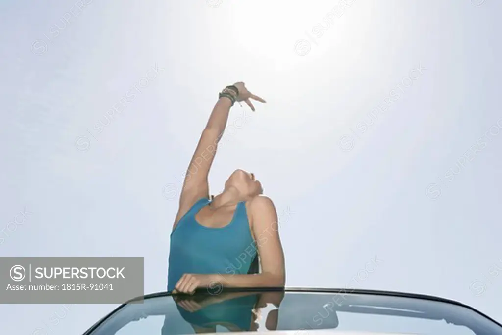 Spain, Majorca, Young woman with victory sign standing in cabriolet car