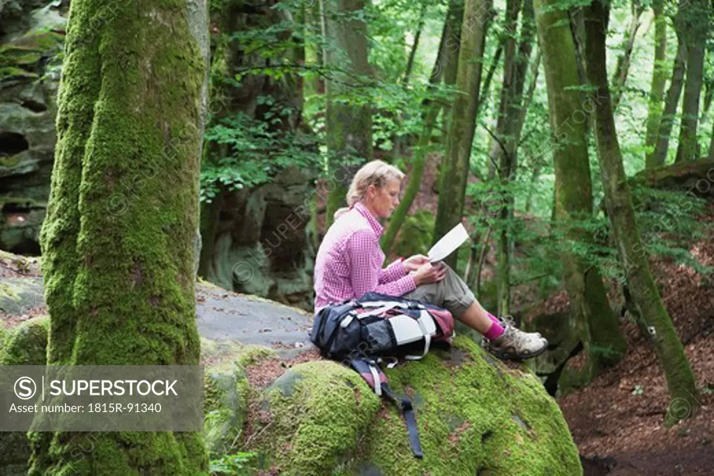 Germany, Rhineland_Palatinate, Eifel Region, South Eifel Nature Park, View of woman hiker sitting on bunter rock formations at beech tree forest