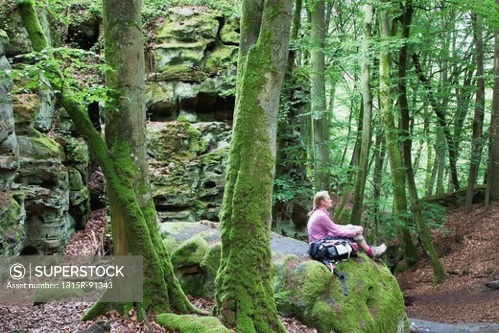Germany, Rhineland_Palatinate, Eifel Region, South Eifel Nature Park, View of woman hiker sitting on bunter rock formations at beech tree forest