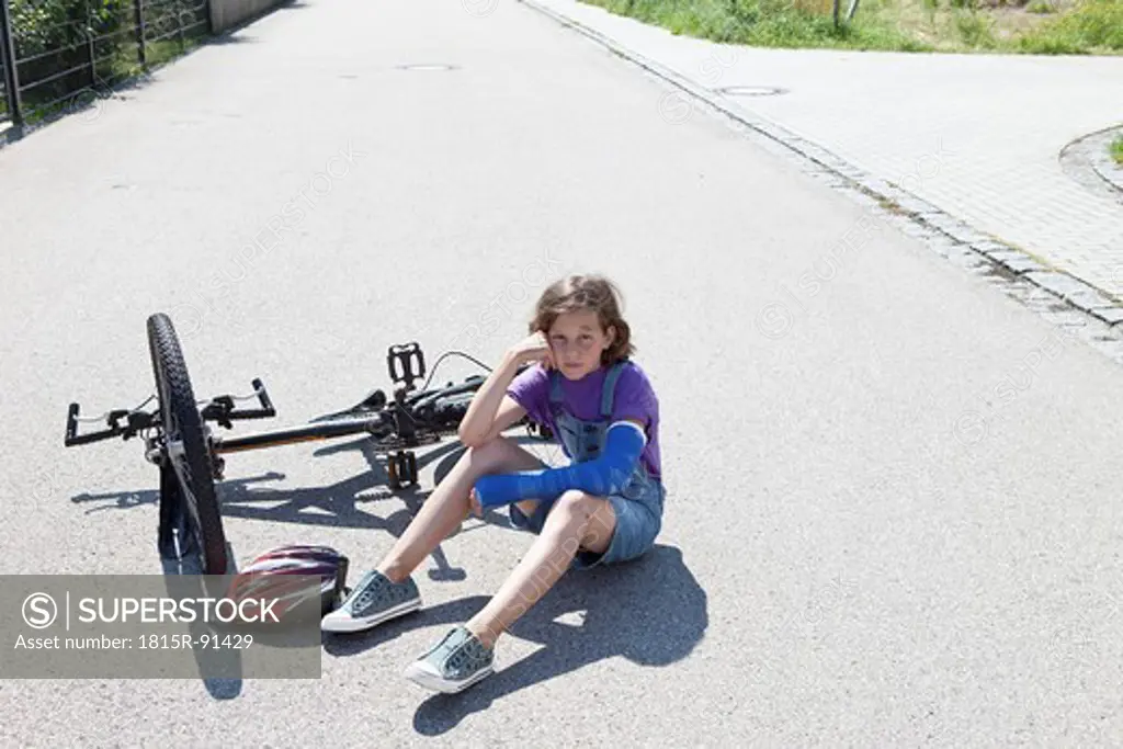 Germany, Bavaria, Wounded girl sitting on road after bicycle accident